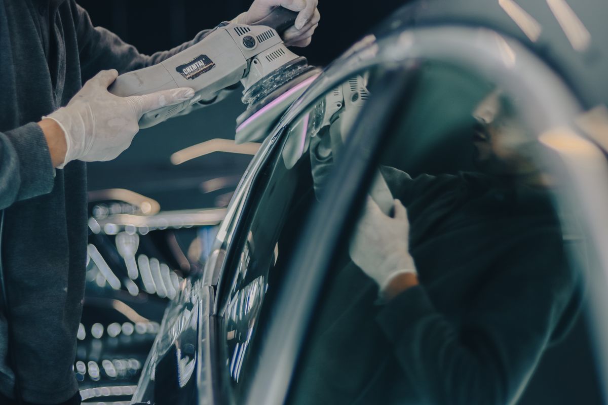Gloved detailer machine-polishing a car’s paintwork in a workshop